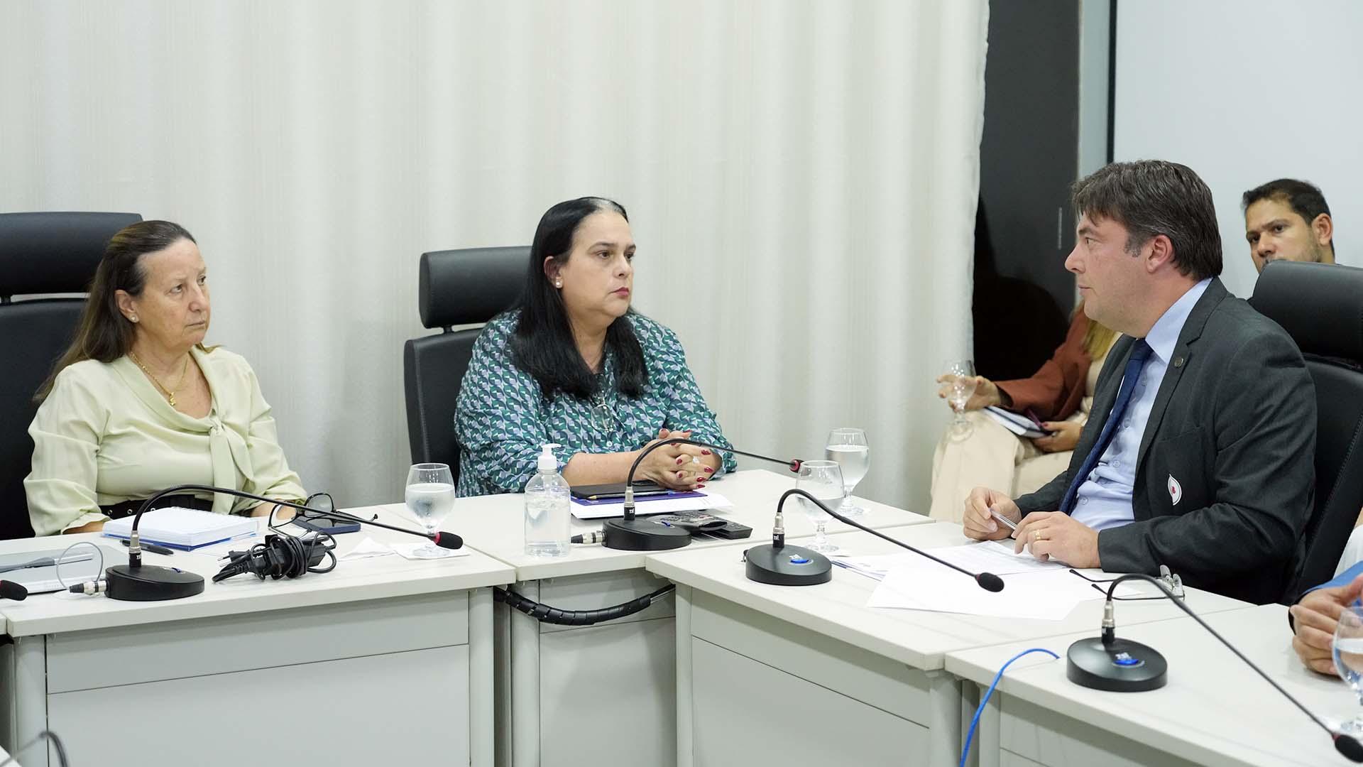 Imagem mostra três pessoas, sendo duas mulheres e um homem, sentadas em torno de uma mesa em reunião. 