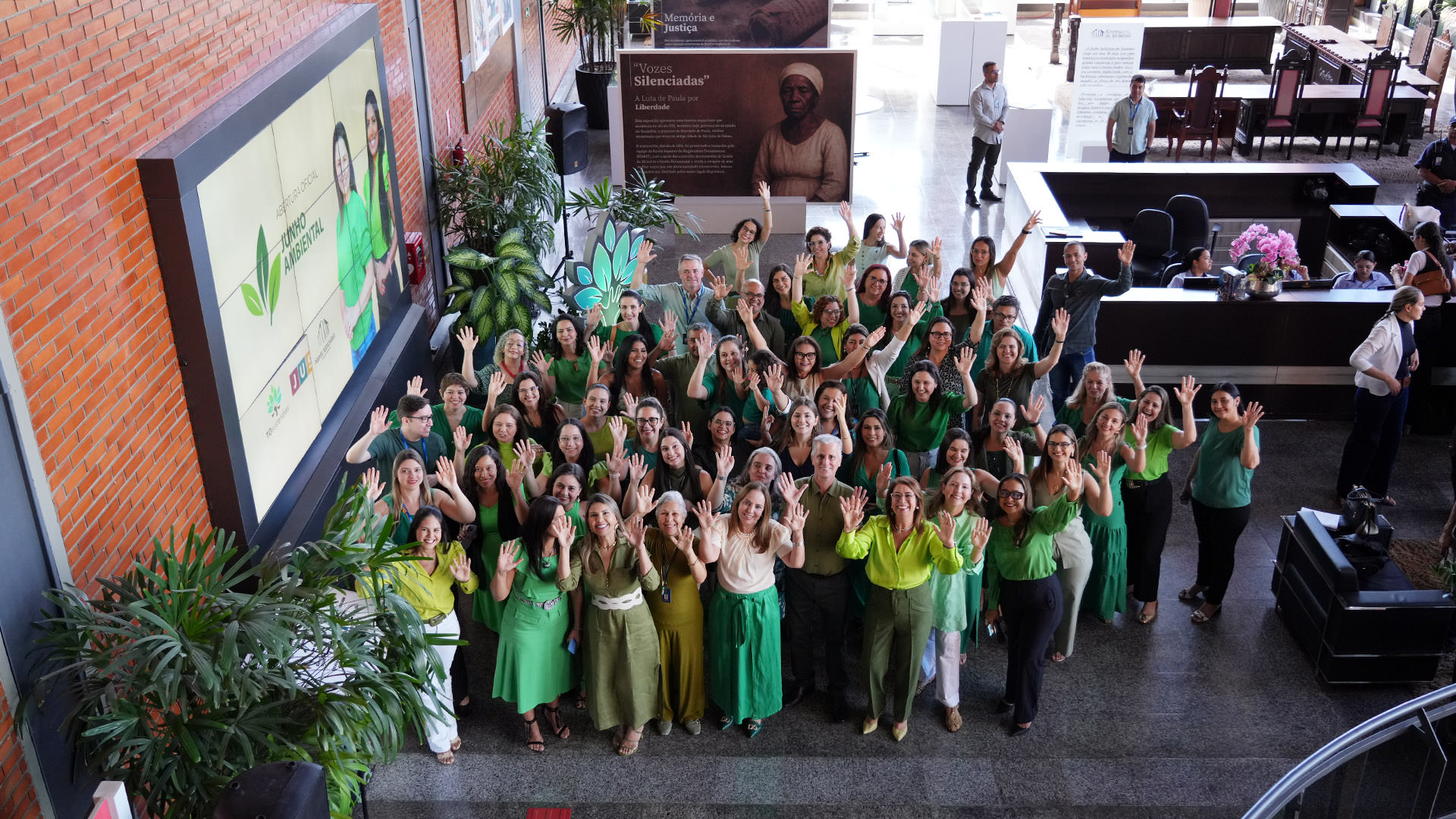 Pessoas vestidas de verde em alusão ao Dia do Meio Ambiente em foto posada com as mãos levantadas 