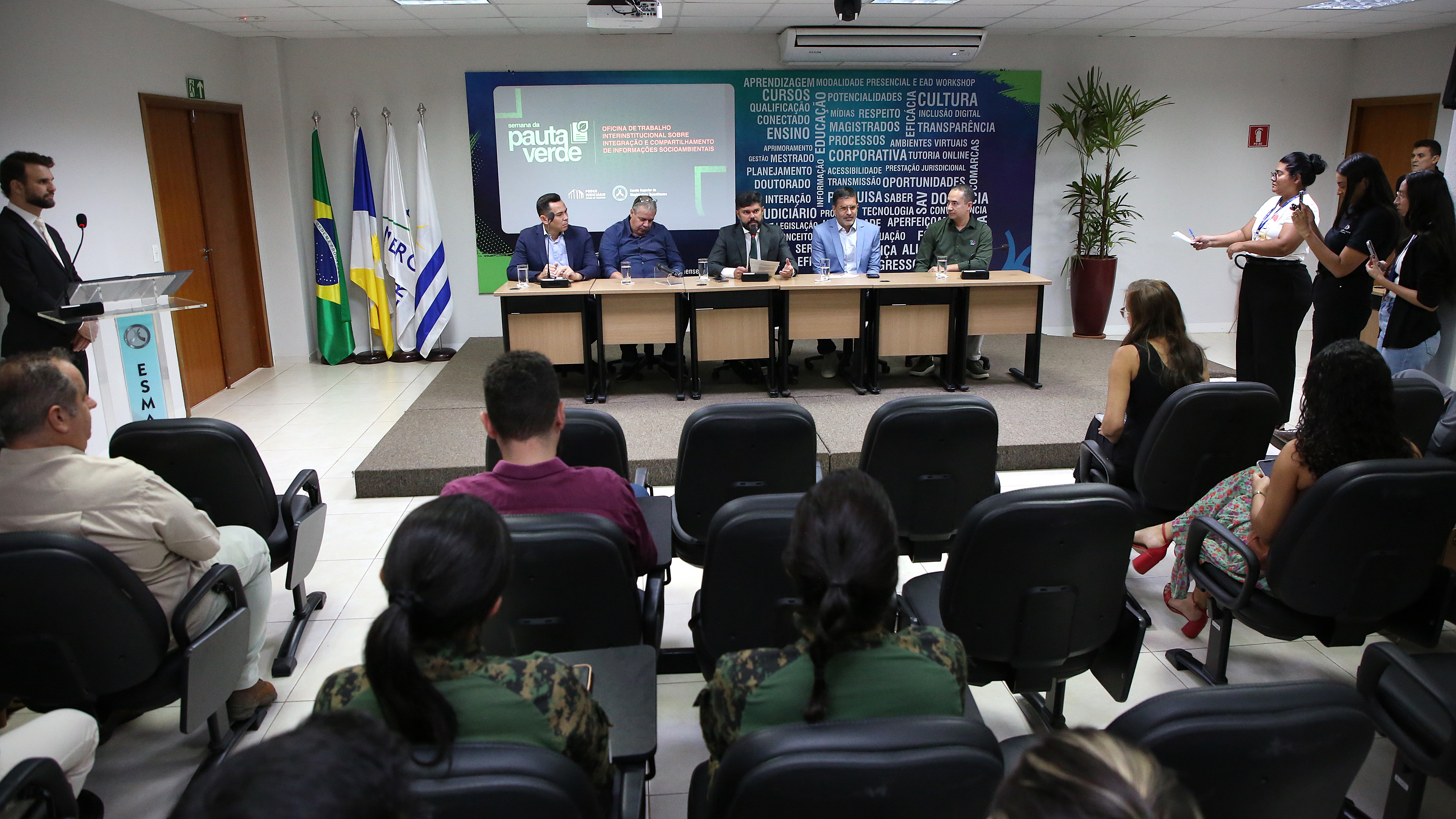 A imagem mostra o auditório da Escola Superior da Magistratura Tocantinense (Esmat) durante a programação da oficina da Semana da Pauta Verde. No espaço, várias pessoas estão sentadas de frente para o palco, onde autoridades compõem a mesa de abertura do evento.