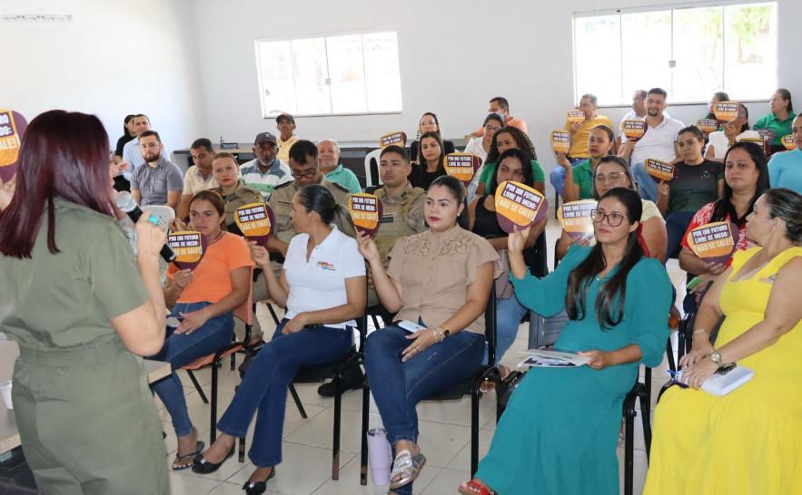 Em uma sala, várias mulheres estão sentadas assistindo a uma palestra e segurando um material publicitário