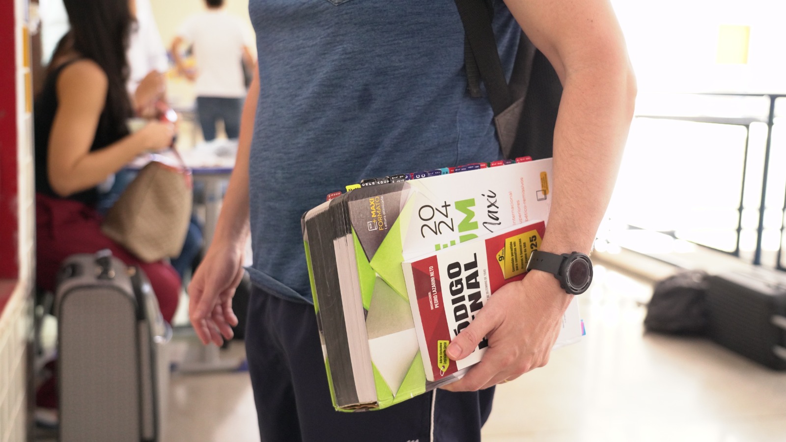 Mão masculina com relógio esportivo segurando livro da área jurídica 
