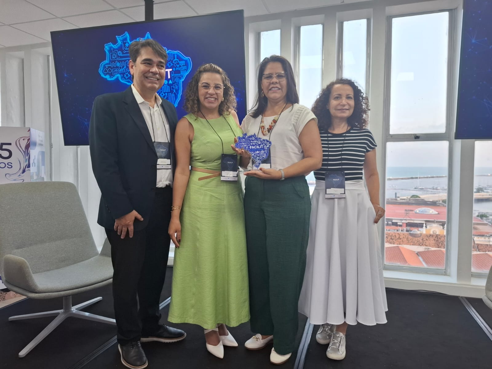 A foto registra um momento de celebração: quatro pessoas posam sorridentes para a câmera em um ambiente de evento. Ao centro, duas mulheres seguram o troféu em acrílico em formato do mapa do Brasil, com a inscrição "Facilit Conectada", prêmio recebido pelo Tribunal de Justiça do Tocantins na área de Gestão Estratégica e Governança.