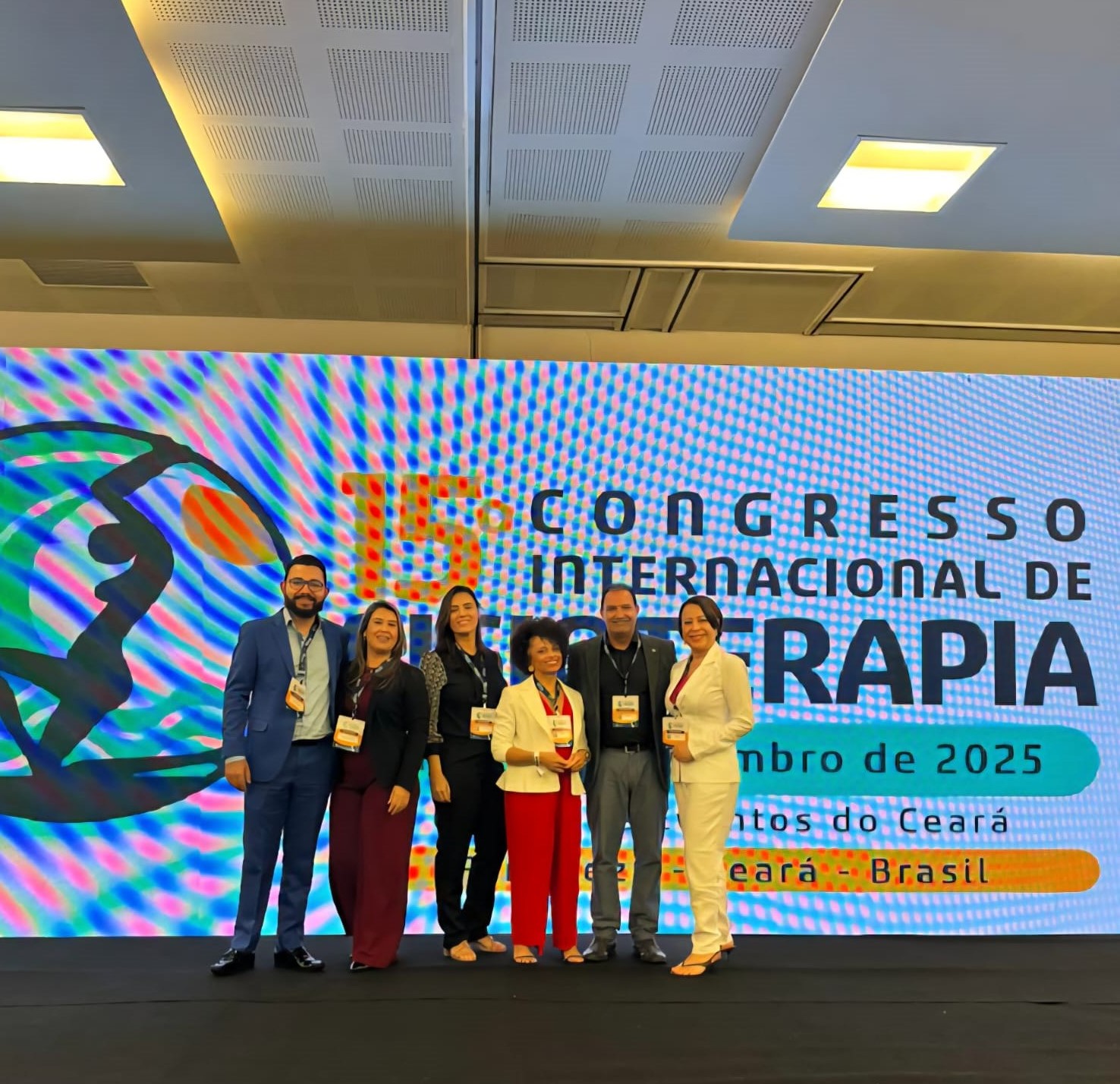 A imagem mostra um grupo de pessoas sorrindo para a foto em um palco, tendo ao fundo um painel com a identificação do 15º Congresso Internacional de Fisioterapia.