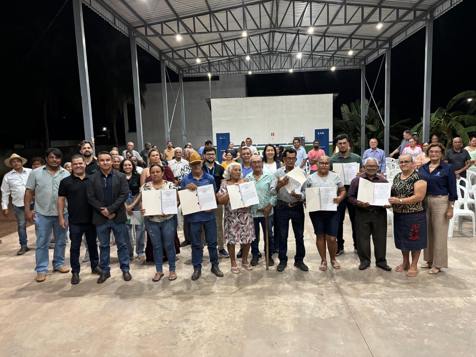 A imagem mostra um grupo de pessoas em área aberta; na frente, algumas delas seguram os títulos de propriedade de seus imóveis.