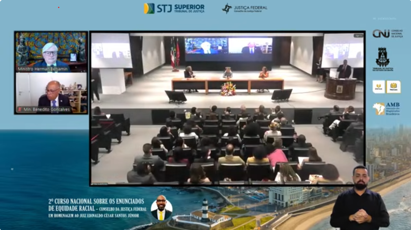  A imagem mostra a transmissão ao vivo pelo YouTube do 2º Curso Nacional sobre os Enunciados de Equidade Racial, com público sentado de costas, palco com três palestrantes, telão ao fundo com dois participantes e intérprete de Libras no canto direito.