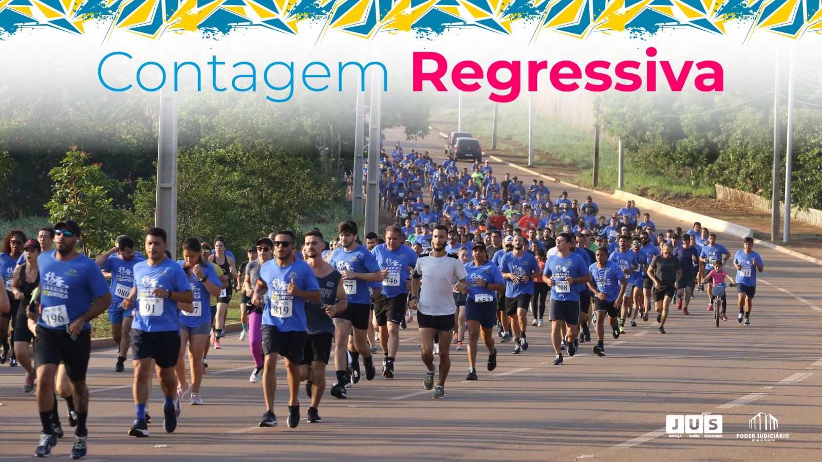  A imagem mostra centenas de corredores vestindo camisetas azuis participando da Corrida da Justiça da Acessibilidade e Inclusão, em uma estrada ensolarada cercada por árvores.