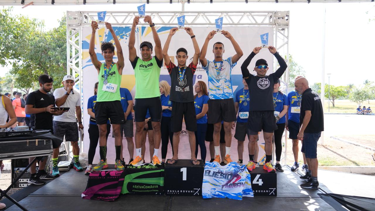 Cinco homens no pódio, com os troféus, celebram a vitória