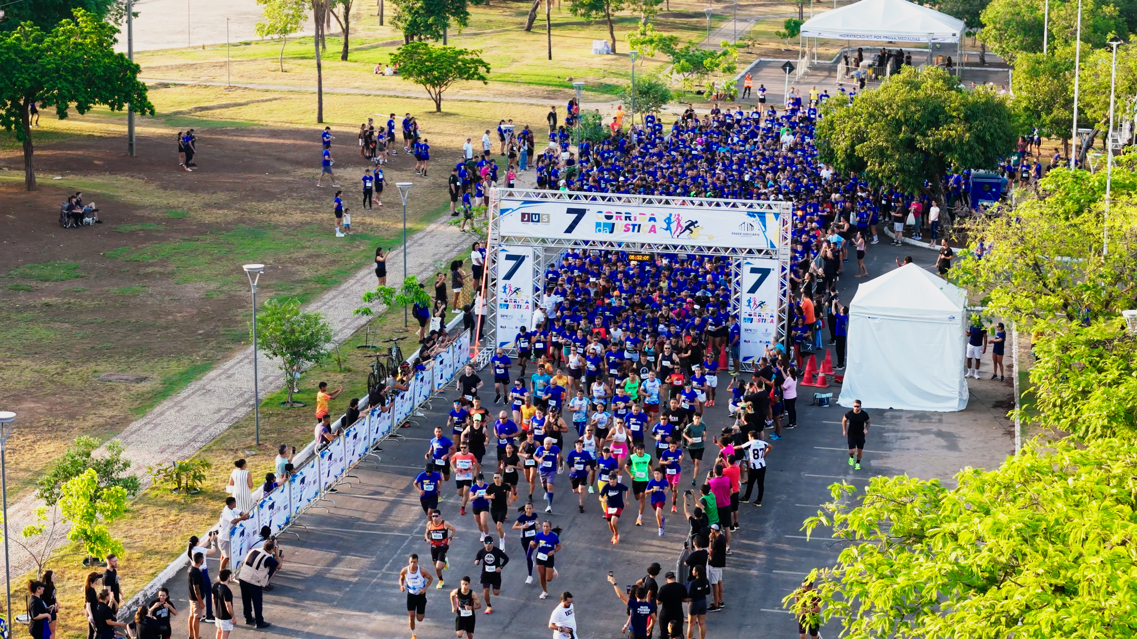 Foto aérea dos corredores após a largada; ao fundo o portal com o nome 7ª Corrida da Justiça