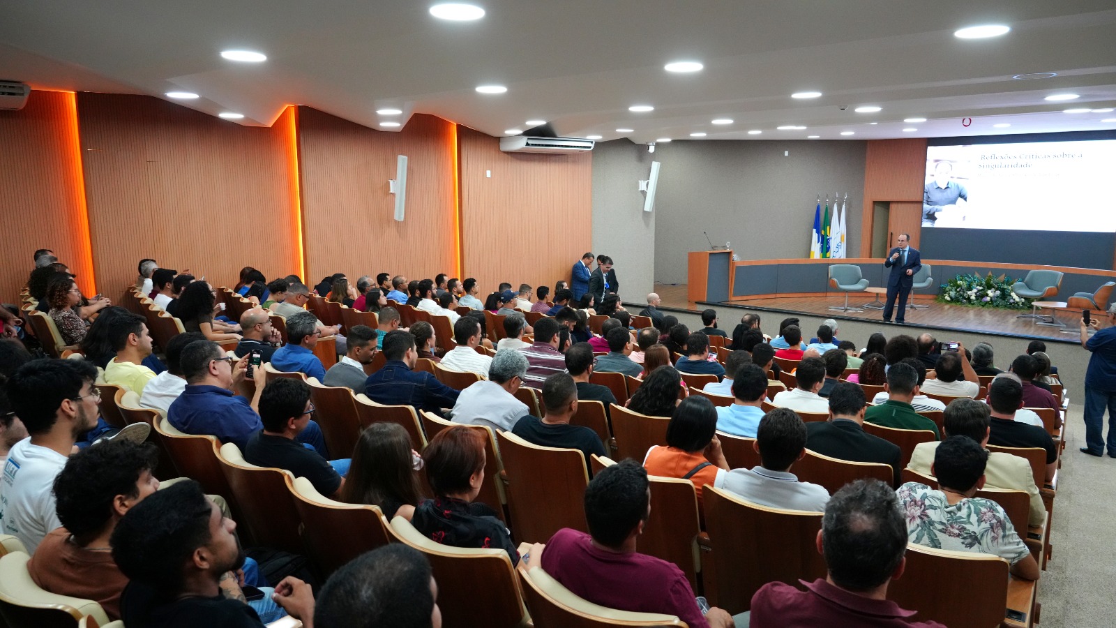 Foto aberta de um auditório lotado e, ao fundo, no palco, o desembargador Marco Villas Boas fala ao microfone