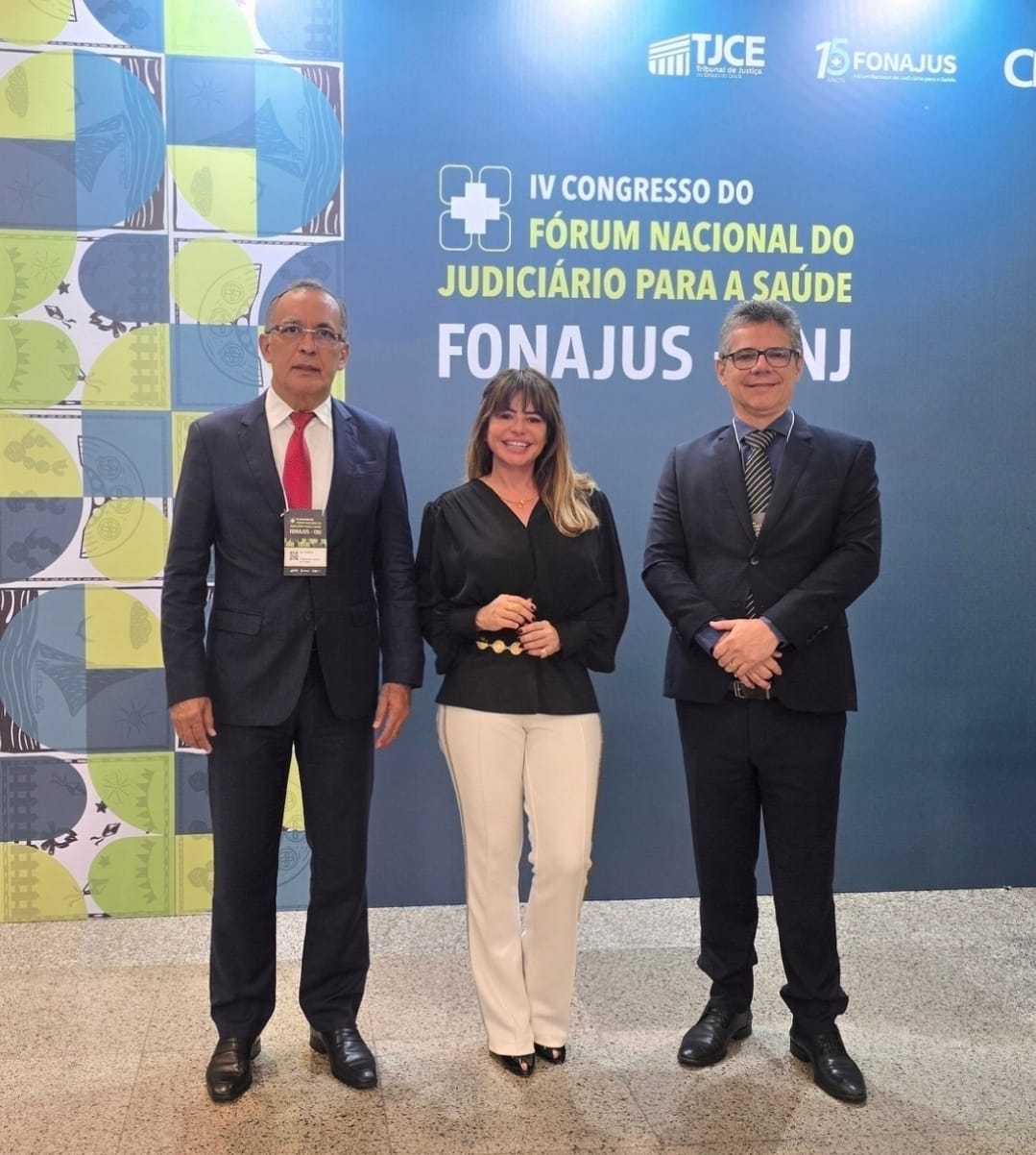 foto mostra três pessoas posando para a câmera em um evento oficial. Ao fundo, há um painel com o texto “IV Congresso do Fórum Nacional do Judiciário para a Saúde – FONAJUS CNJ