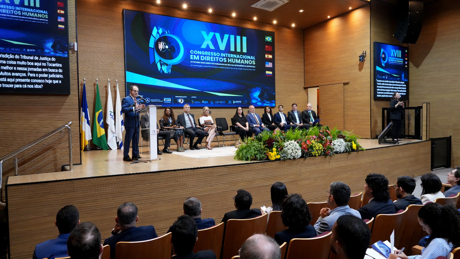 Foto mostra a abertura do congresso no auditório do TJTO, com o desembargador Marco Villas Boas no púlpito, autoridades no palco e público assistindo.