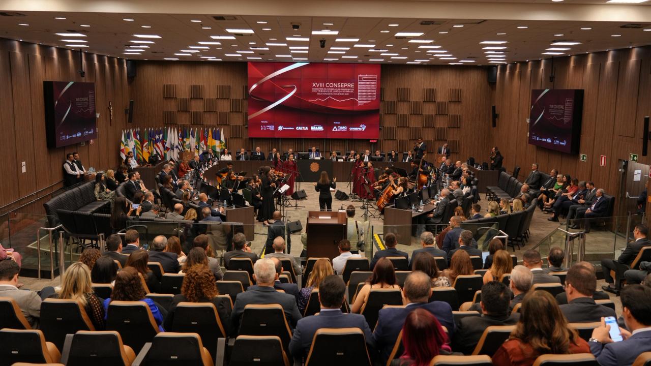 Auditório cheio durante o XVIII CONSEPRE, com orquestra se apresentando no centro e autoridades reunidas na mesa principal ao fundo.