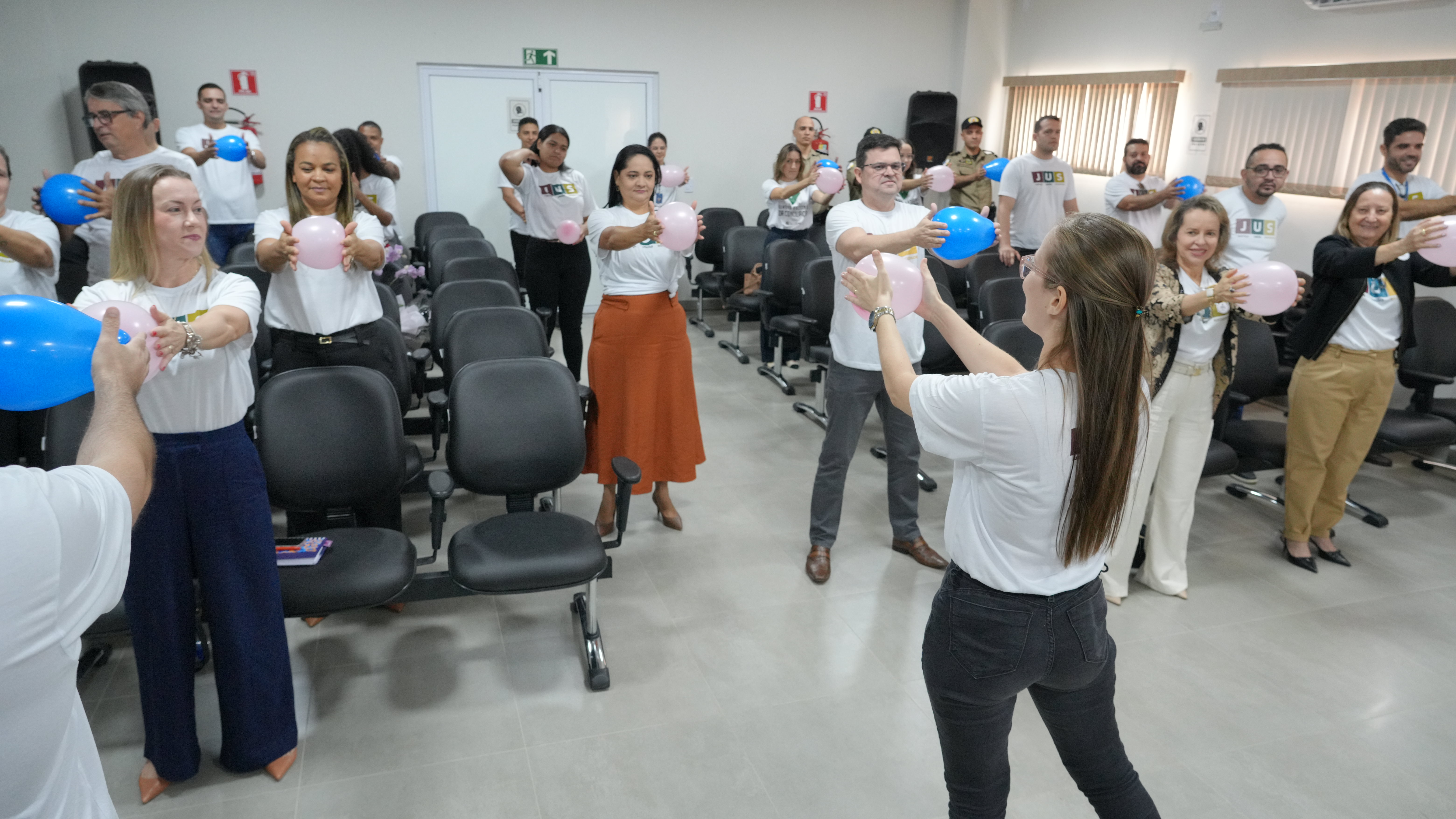 Foto aberta com várias pessoas em pé com balão nas mão praticando ginástica laboral