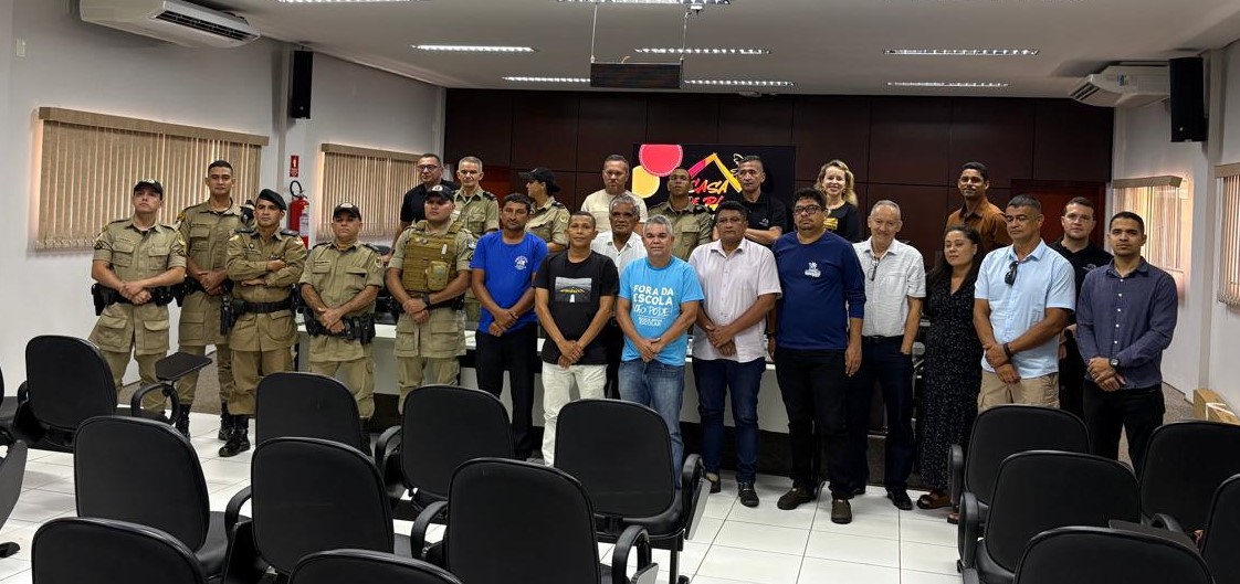 A imagem mostra um grupo de pessoas em um auditório, com cadeiras ao fundo. À esquerda, policiais militares fardados; ao centro e à direita, servidores e representantes civis, em trajes sociais e casuais. A imagem registra um encontro institucional.