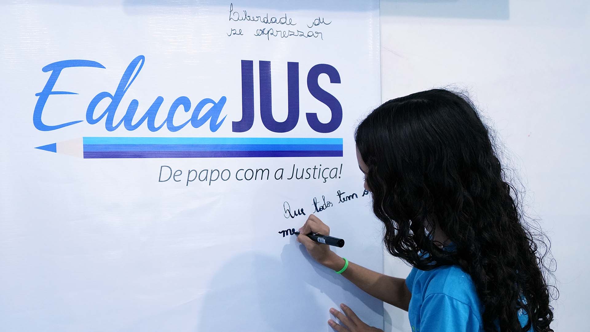 Criança escreve em um painel branco com a marca “EducaJus – De papo com a Justiça!”