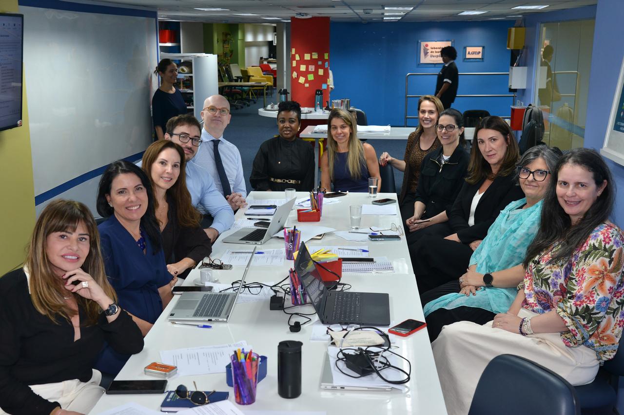 A imagem mostra a juíza Milene de Carvalho Henrique e demais participantes reunidos em mesa de trabalho durante oficina nacional sobre regulamentação e aprimoramento do Núcleos de Apoio Técnico do Judiciário (NatJus)..
