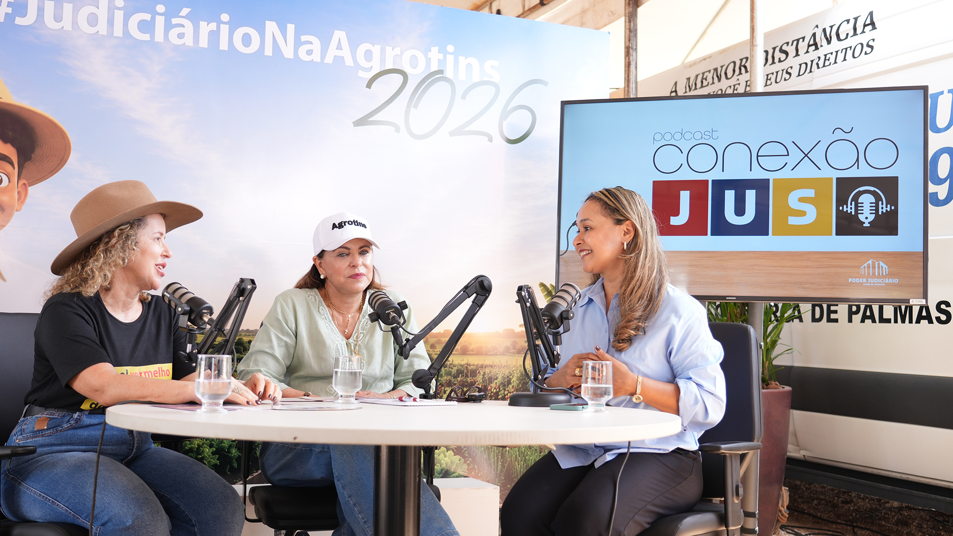 A desembargadora Ângela Prudente, ao centro, e a juíza Cirlene Maria de Assis, à esquerda, participam de gravação do podcast “Conexão JuS” no estande do Poder Judiciário do Tocantins durante a Agrotins 2026. O episódio abordou enfrentamento à violência contra a mulher, acolhimento e conscientização, em conversa mediada pela jornalista Betânia Sousa.