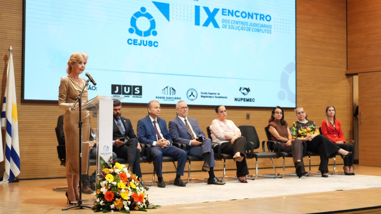 A desembargadora Silvana Maria Parfieniuk fala ao microfone durante a abertura do VIII Seminário sobre Políticas Públicas de Tratamento Adequado de Conflitos e IX Encontro dos Cejuscs, no auditório do TJTO. Ao lado, autoridades acompanham a solenidade no palco do evento.