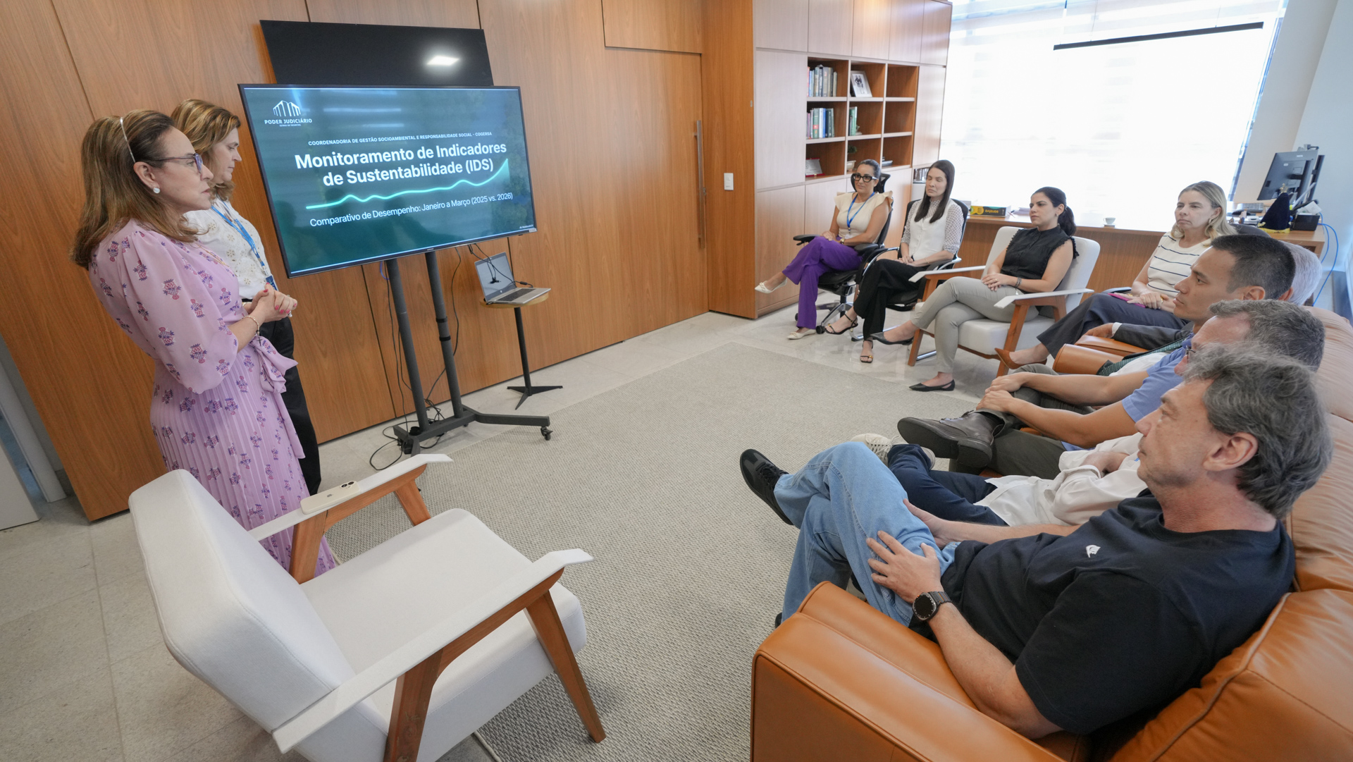 A imagem mostra equipe da gestão socioambiental do TJTO durante visita institucional em gabinete, apresentando indicadores de sustentabilidade e ações de conscientização a magistrados e servidores.  Os participantes estão sentados e atentos à apresentação exibida em tela sobre monitoramento do Índice de Desenvolvimento Sustentável (IDS) do Tribunal.