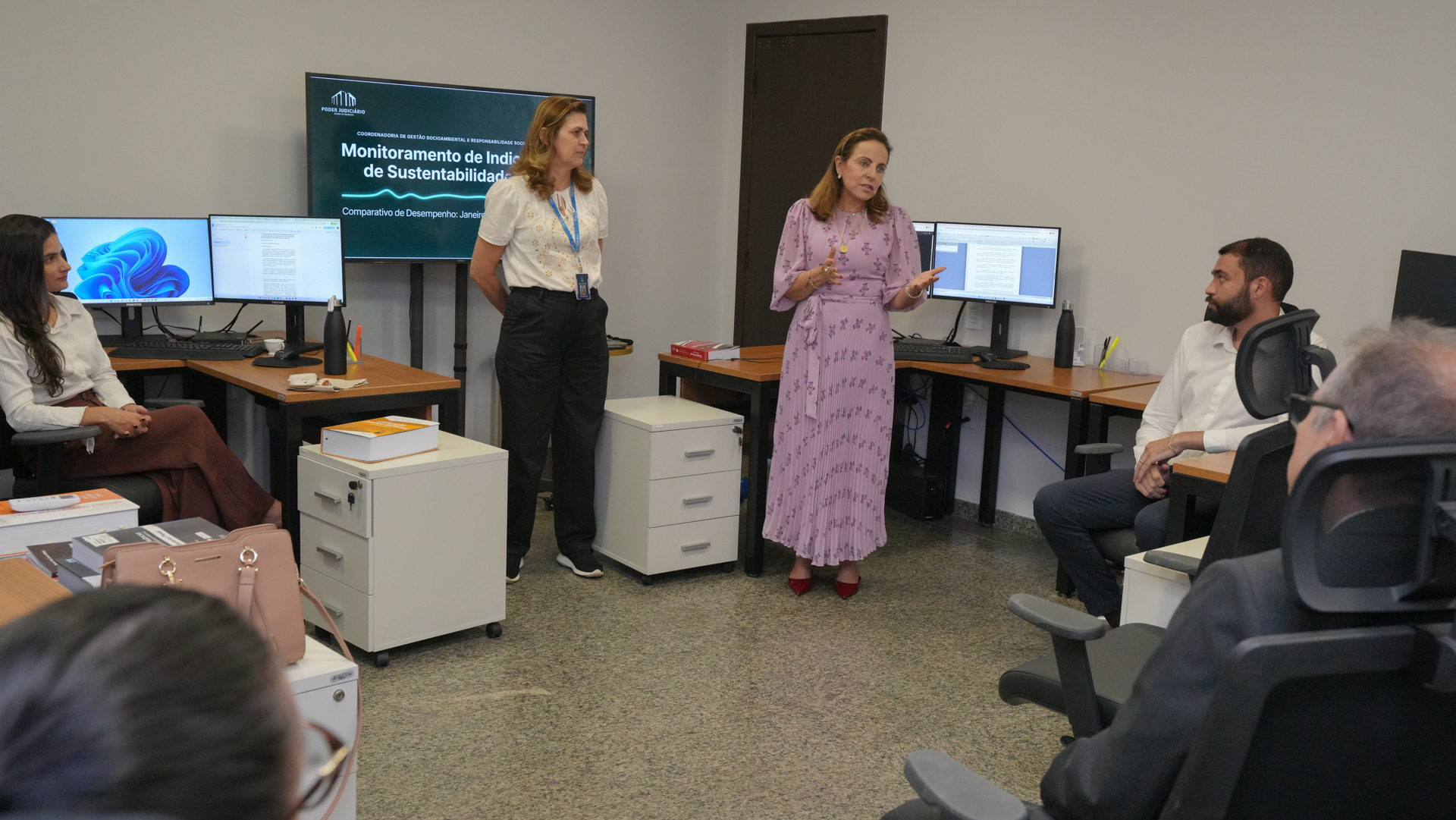 A imagem mostra equipe da gestão socioambiental do TJTO realizando apresentação sobre indicadores de sustentabilidade em ambiente de gabinete, com servidores e magistrados acompanhando atentamente a exposição.