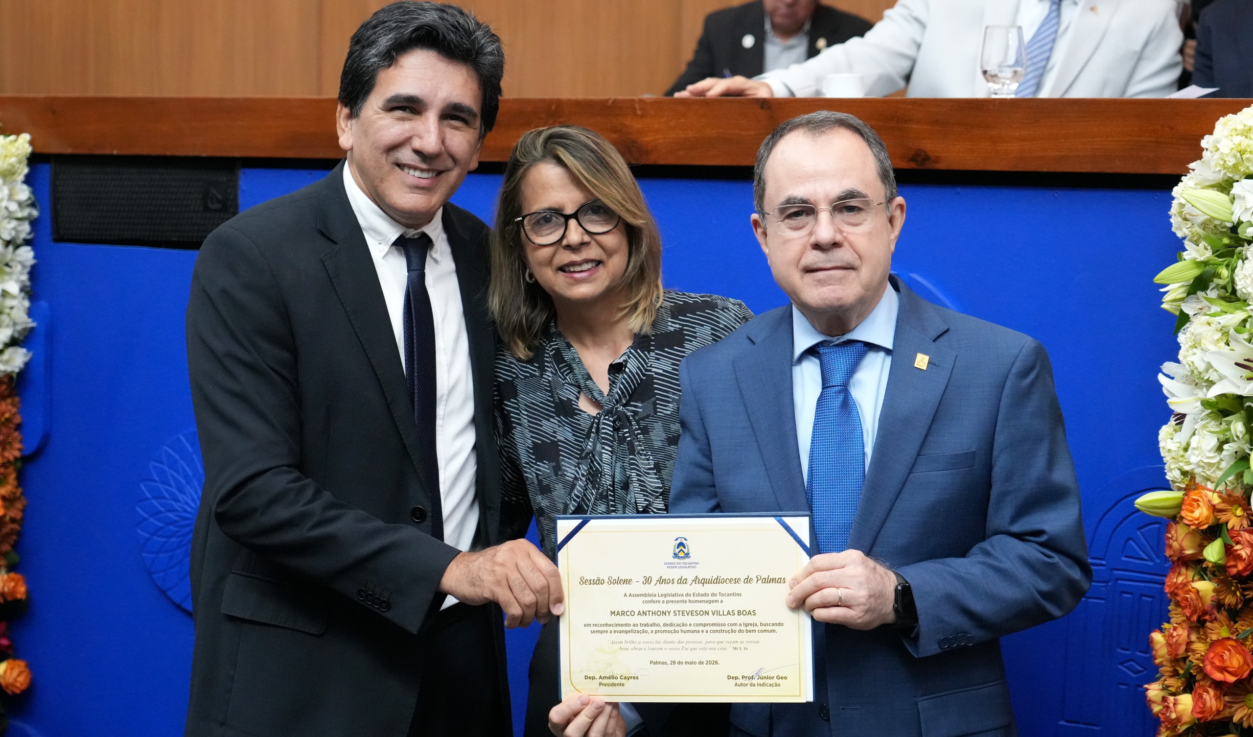 A imagem mostra o desembargador Marco Anthony Steveson Villas Boas sendo homenageado durante uma sessão solene, ao lado de outras autoridades, enquanto recebe um certificado de reconhecimento.
