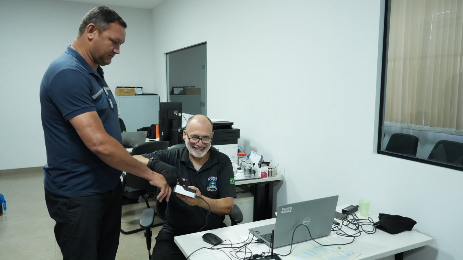 A imagem mostra atendimentos realizados durante o projeto Jus em Ação, com equipe técnica prestando suporte e serviços à população em um ambiente preparado para a ação. Em destaque, dois participantes interagem em frente a um computador durante a coleta biométrica.