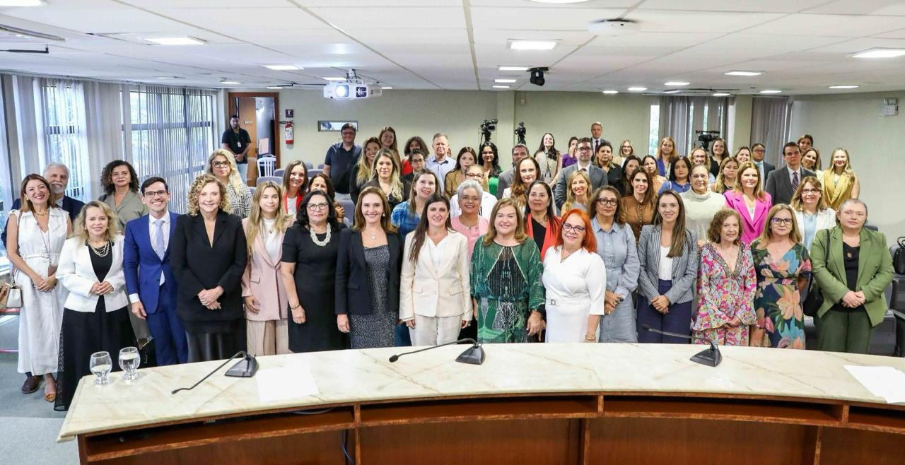 A imagem mostra várias pessoas em pé durante a cerimônia de posse da XVIII Comissão do Fórum Nacional de Juízas e Juízes de Violência Doméstica e Familiar contra a Mulher.