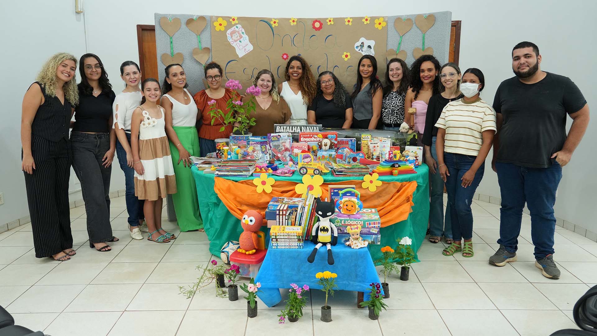 A imagem mostra um grupo de pessoas reunidas atras de uma mesa cheia de brinquedos, livros infantis e jogos educativos durante a entrega de itens da campanha do TJTO ao Centro de Atendimento Integrado. 
