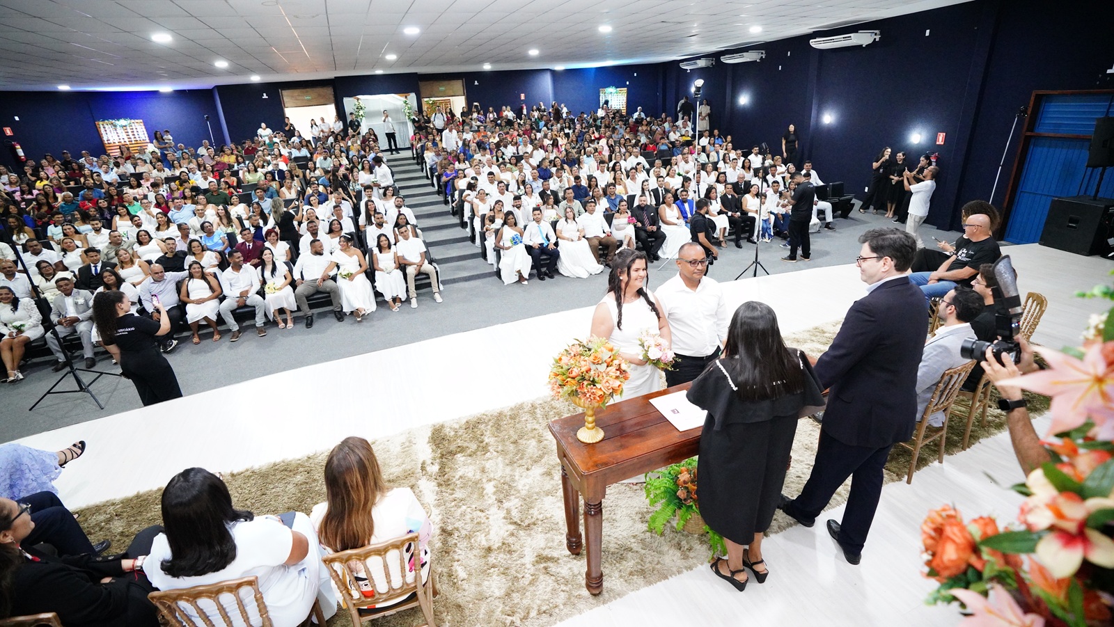 Imagem mostra um auditório visto do fundo do palco repleto de casais e familiares do casamento comunitário realizado em Araguaína