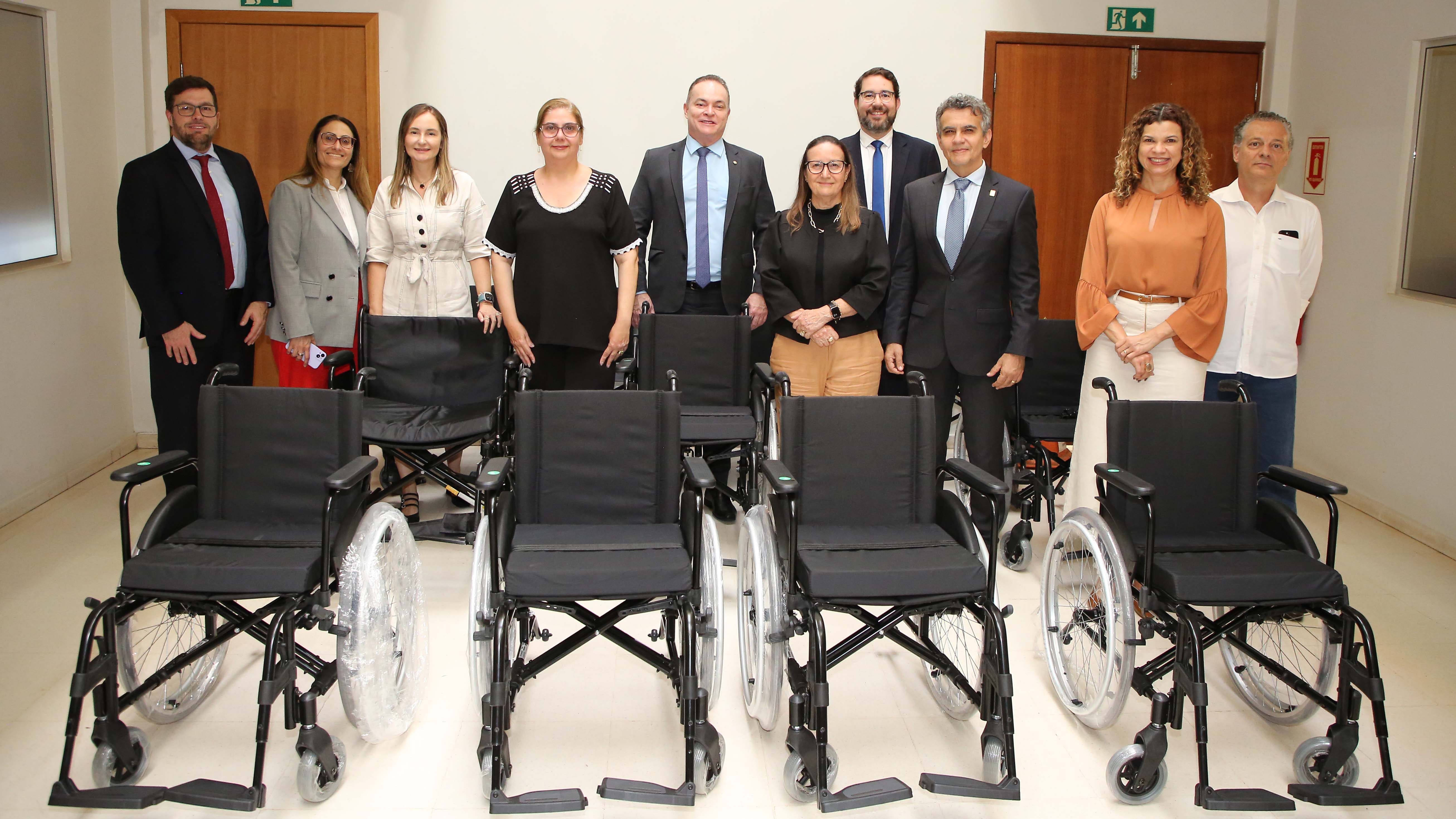 Grupo de dez pessoas posando para foto. À frente delas há sete cadeiras de rodas novas. O grupo é composto por homens e mulheres vestidos com trajes sociais.