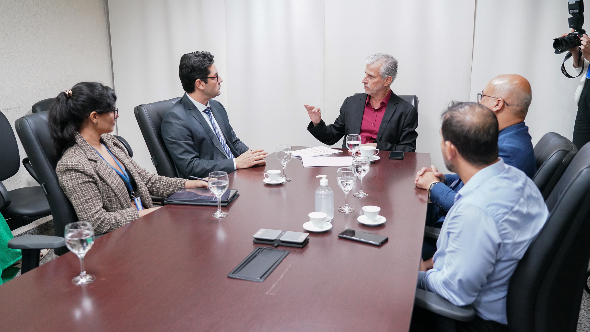 Foto aberta de uma reunião em que estão reunidas cinco pessoas, ao centro, o juiz auxiliar da Presidência, Esmar Custódio, um homem branco de cabelos grisalhos, usando um blazer preto e camisa vermelha; ao seu lado esquerdo uma mulher e um homem, e à direita dois homens 