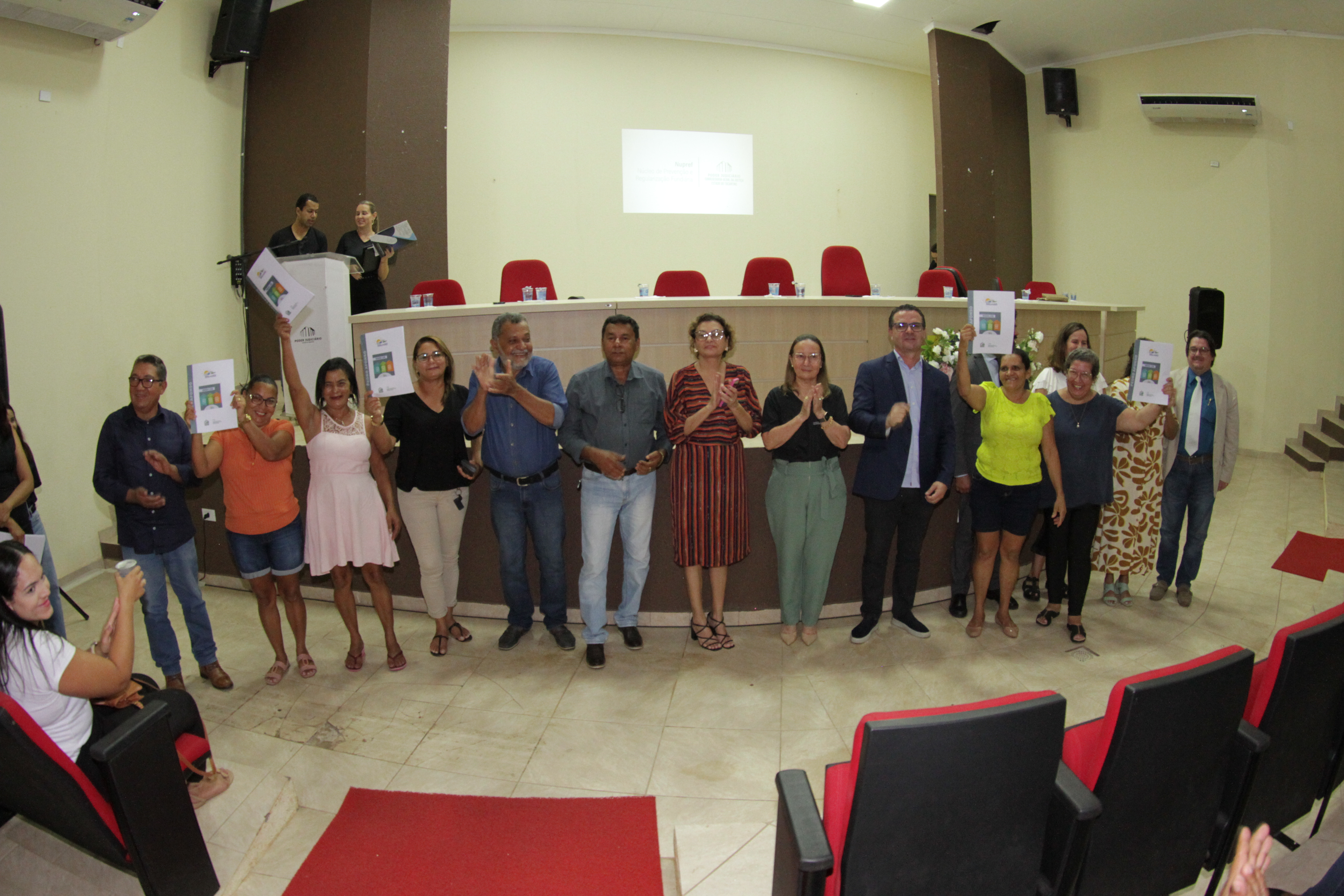 Pessoas posam para foto, algumas seguram um documento para cima e outras batem palmas