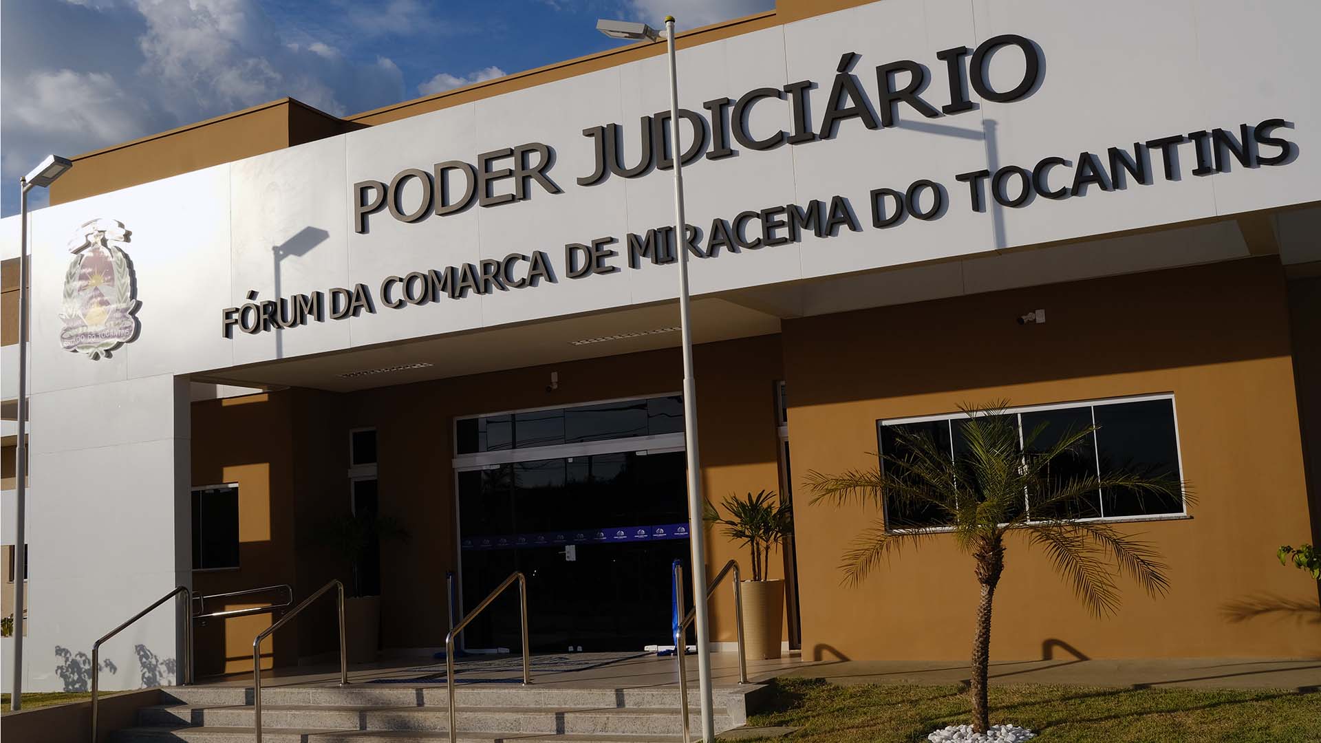 Prédio do Fórum de Miracema visto de frente, com parte da escada, paredes pintadas de marrom e fachada branca com letreiros na cor preta