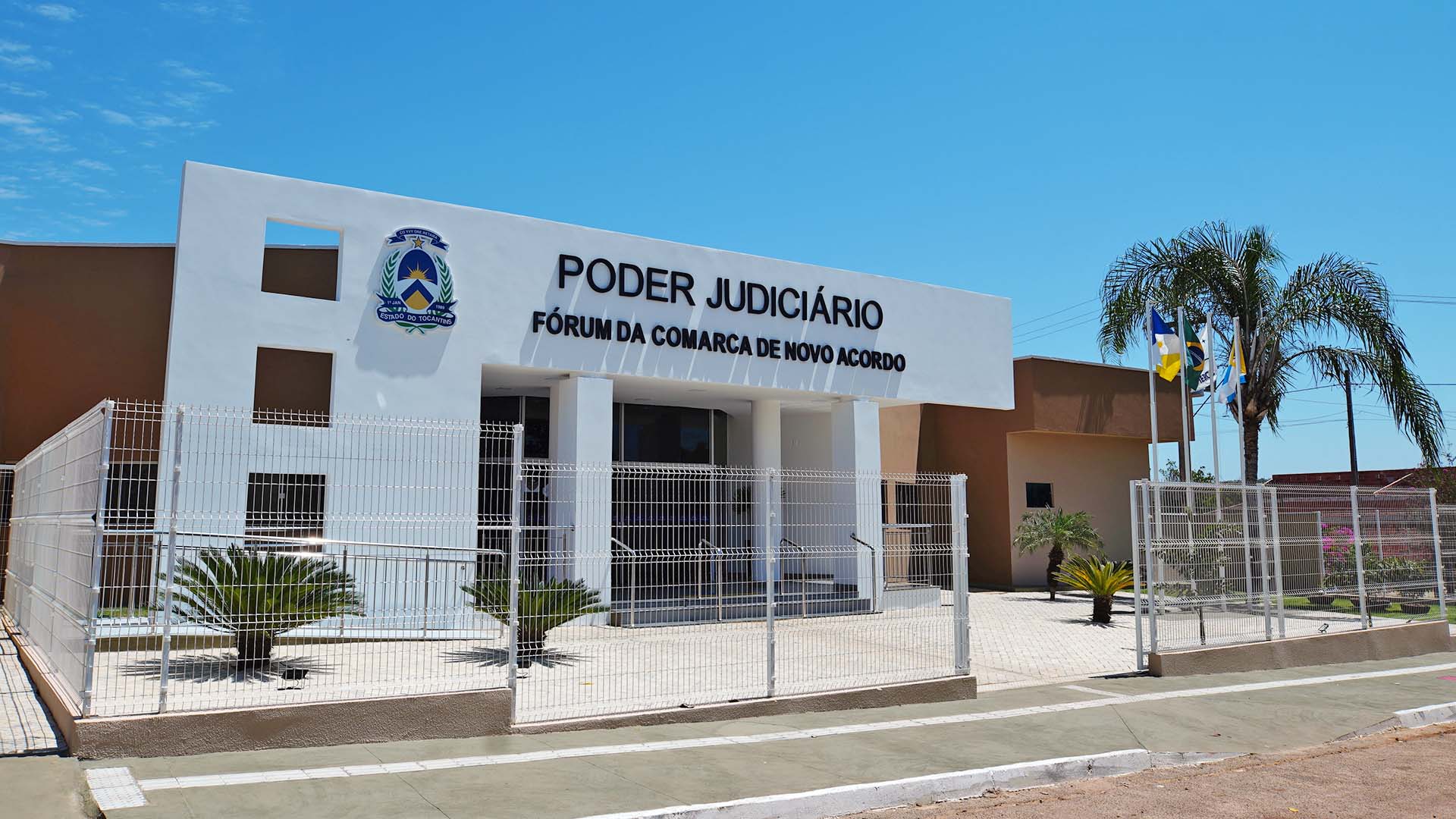 Fachada principal do fórum de Novo Acordo, na cor branca. O prédio tem a cor marrom e possui cerca de segurança