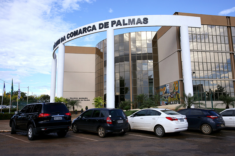 Fachada do fórum de Palmas com os arcos e colunas à frente e parte do estacionamento lateral com carros estacionados