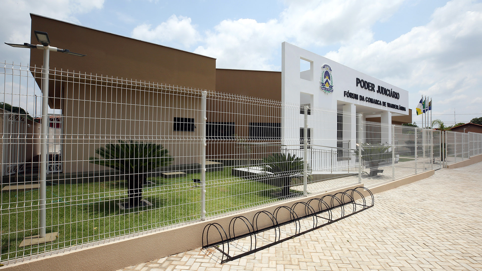 Fachada lateral do Fórum de Wanderlândia mostra o prédio com paredes na cor marrom e pórtico na cor branca com letreiro na cor preta, grades de proteção e bicicletário na calçada