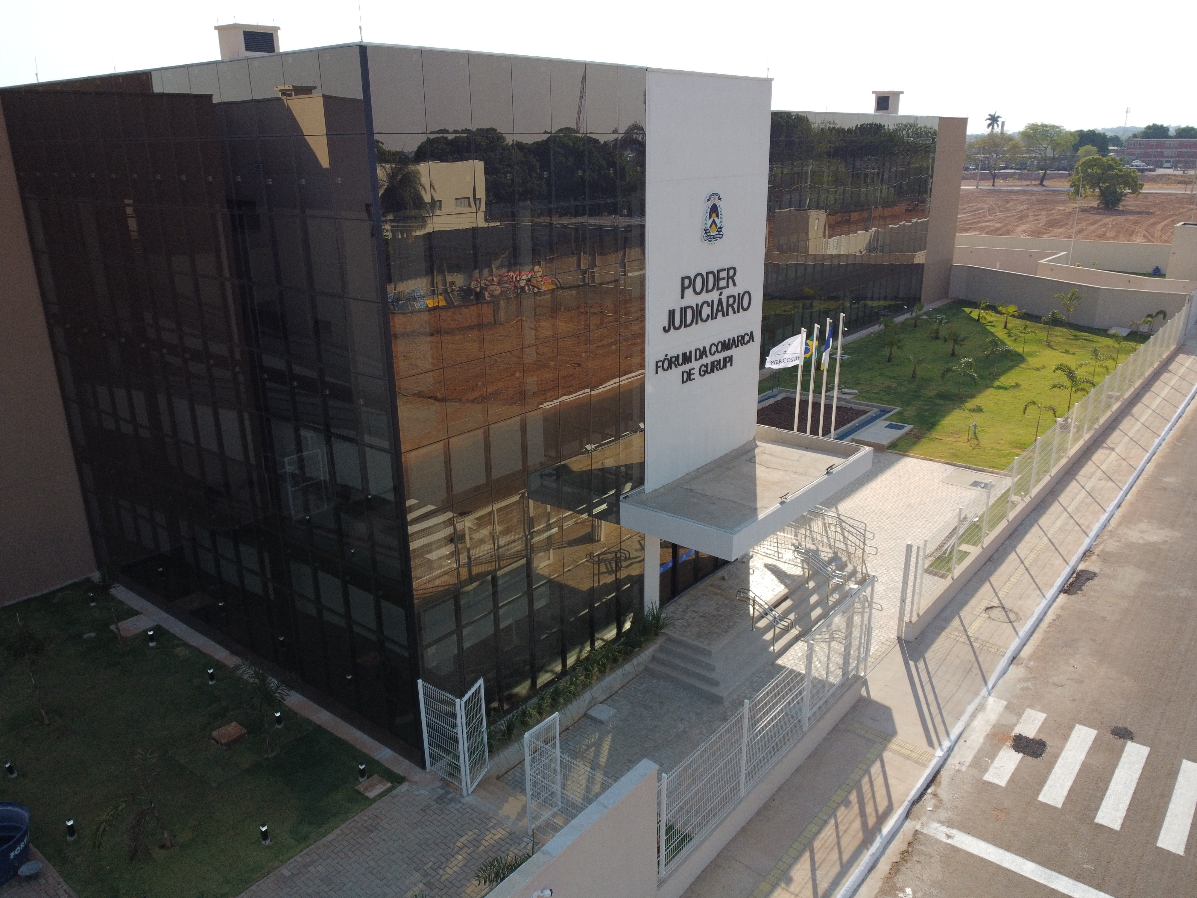 Fachada do prédio do Fórum de Gurupi, da perspectiva lateral, com vista das colunas e fachada na cor marrom e paredes vermelhas, janelas com vidraças escutas e calçada