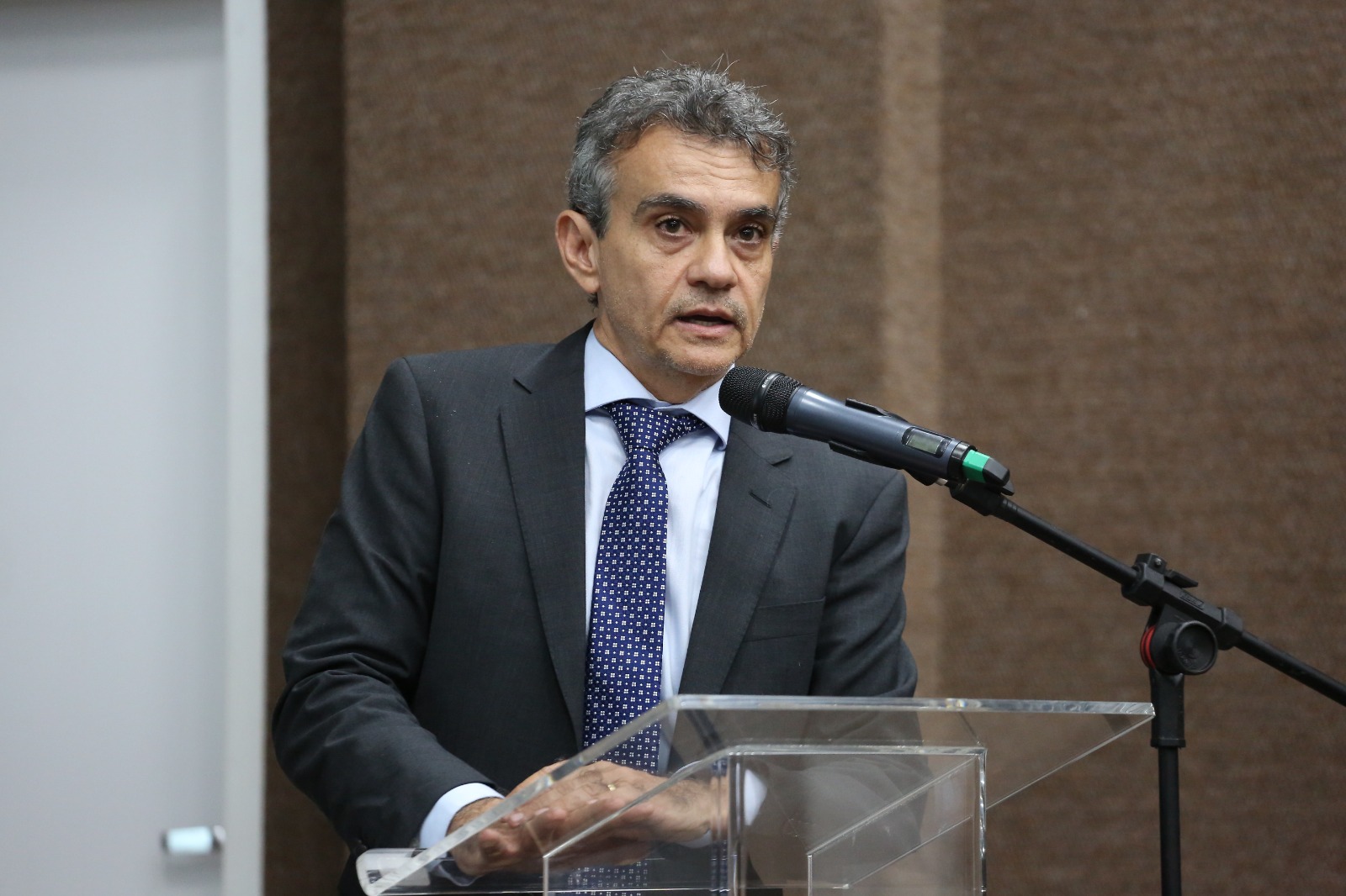 Homem branco grisalho com terno preto fala ao microfone