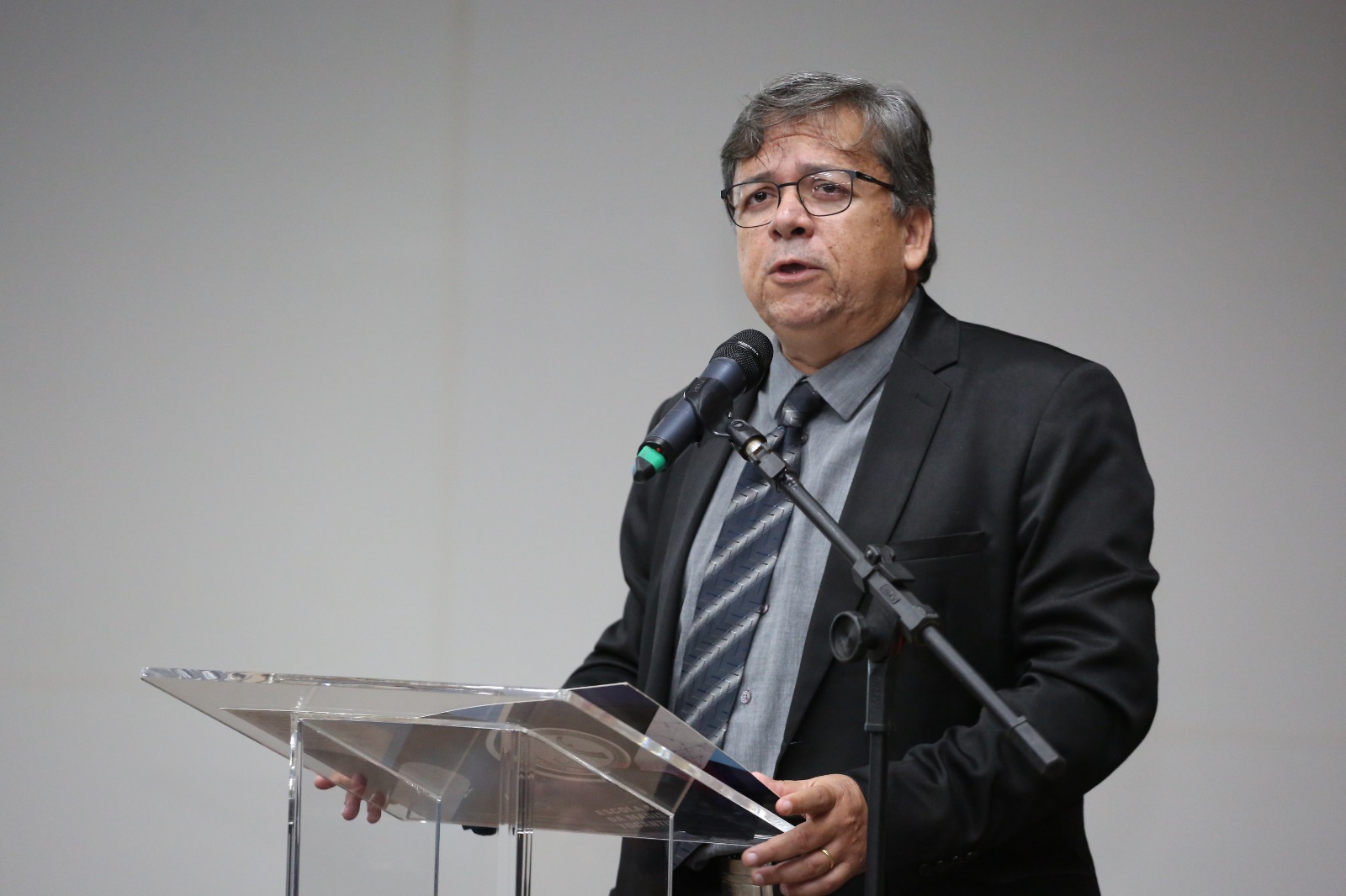 Homem de terno cinza grisalho com óculos fala ao microfone