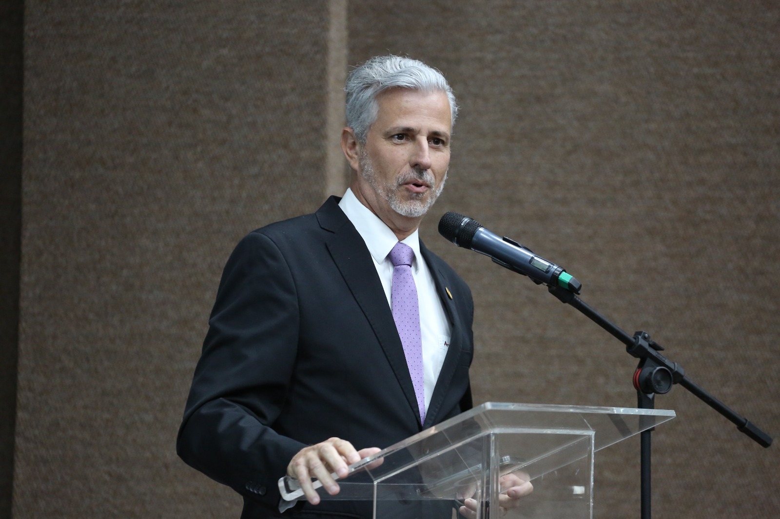 Homem grisalho e terno preto fala ao microfone