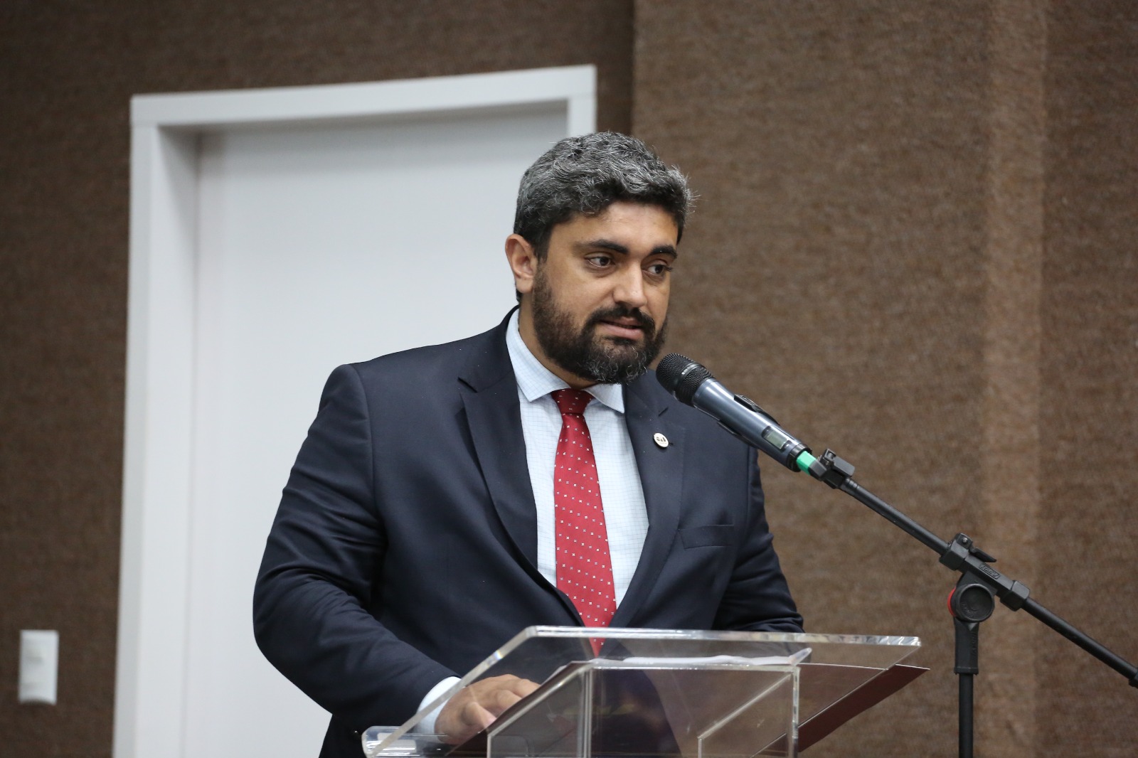 Homem com cabelo preto grisalho e terno preto fala ao microfone