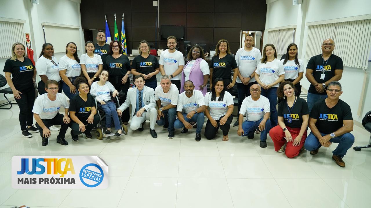 Grupo de pessoas reunidas posando para foto algumas estão usando camisetas pretas e outras brancas. No fundo, há bandeiras institucional,