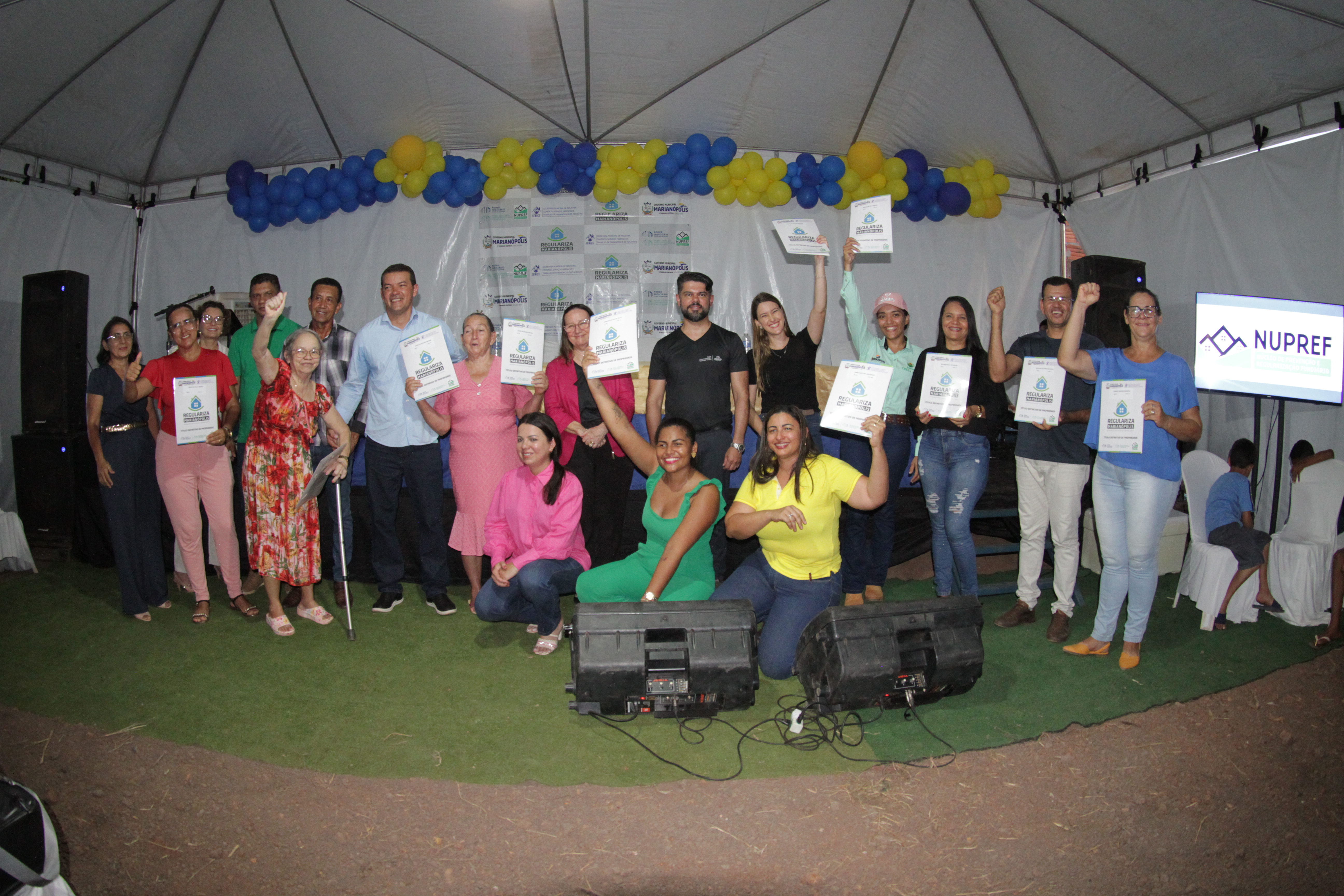 Pessoas posam para foto, algumas seguram um documento para cima e outras sorriem para foto