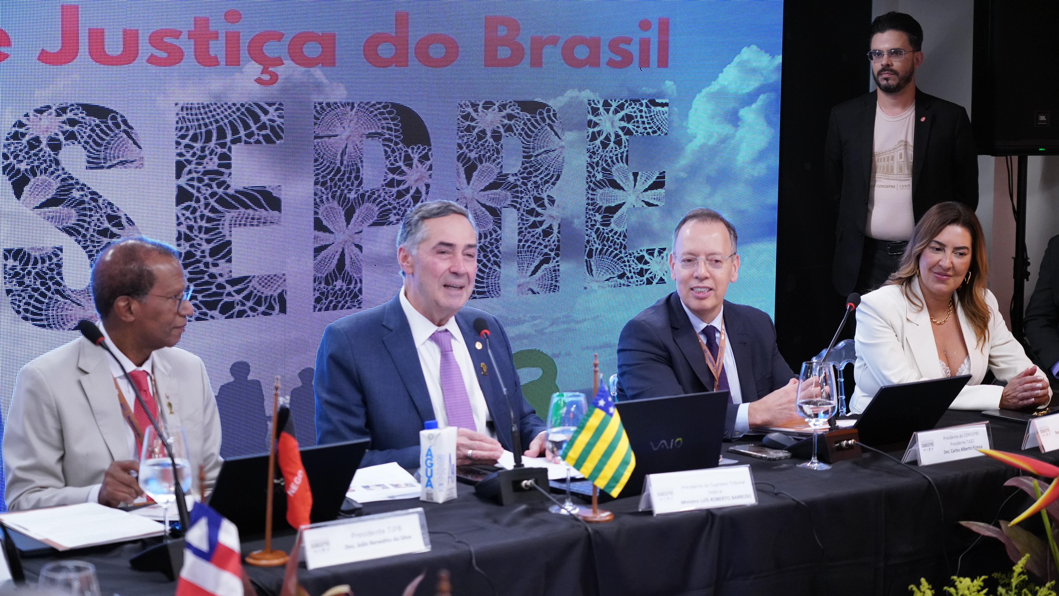 ministro Barroso, ao centro, está sentado ao lado de dois desembargadores, usa terno azul, camisa branca e gravata lilás