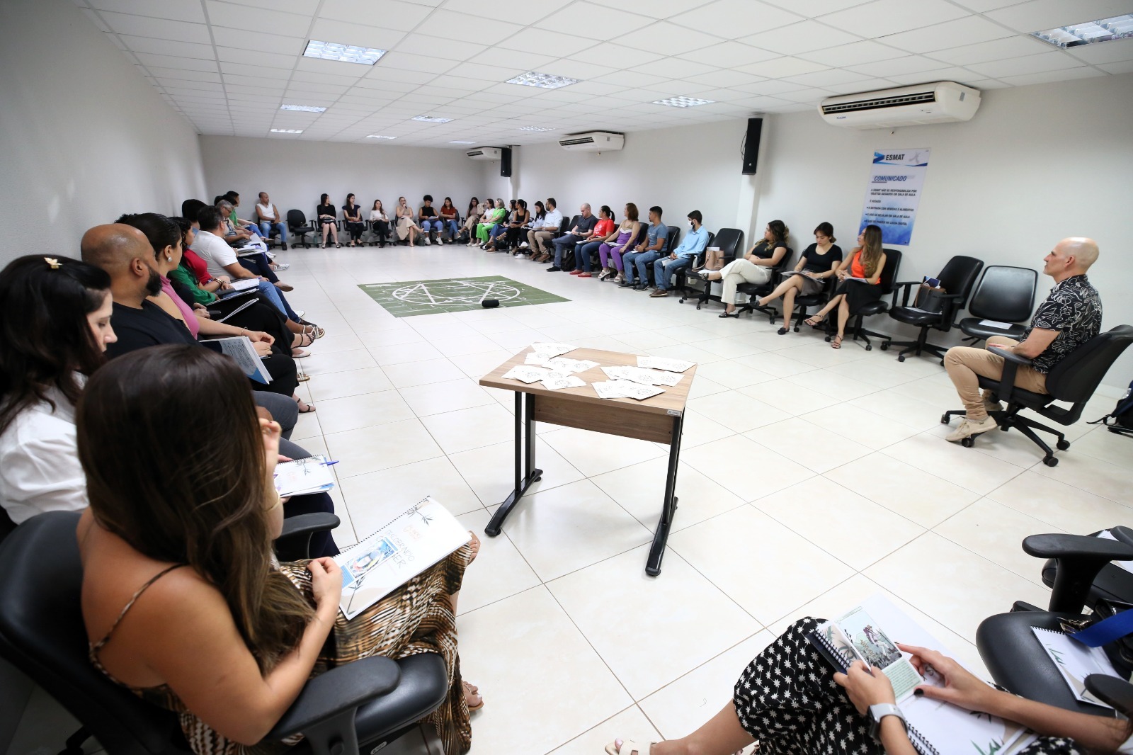 Foto de uma sala de aula com alunos e instrutor sentados em roda, conversando