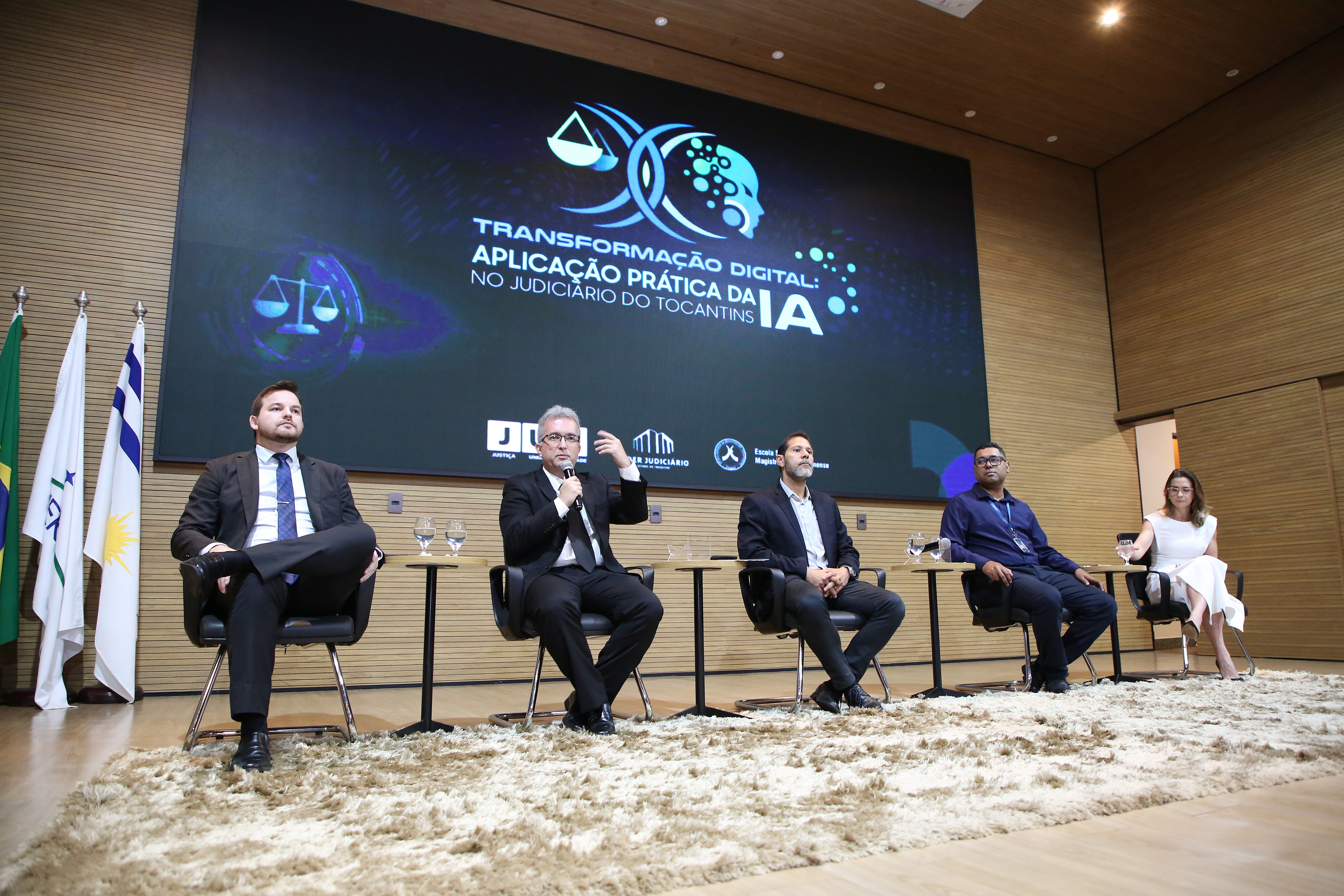 Imagem mostra quatro homens e uma mulher sentadas em cadeira perfiladas no pauco do auditório do TJTO durante encontro sobre inteligência artificial